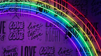 A neon rainbow lights up a wall with "love" written on it multiple times.