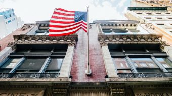 View from below of a flag hanging from a pole on a building.