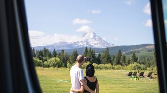 View from a car window of a man and woman standing with their arms around each other gazing at a mountain.