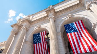 View from the ground of a building showing large American flags hanging down.