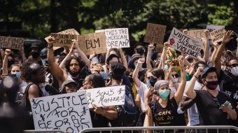 Protesters hold up signs while standing before barricades.