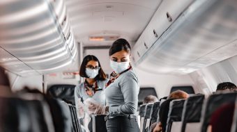 Two flight attendants wearing masks aboard a crowded plane.