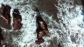 Waves splash against rocks in a turbulent body of water.