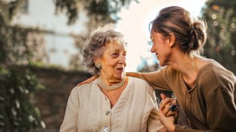 A woman sits talking with a senior woman, with her arm on her shoulder.