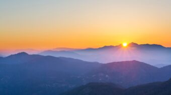 sunrise peaking over foggy blue mountains